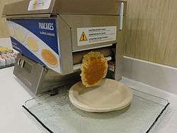 A Quickcakes pancake machine ejecting a finished pancake onto a plate