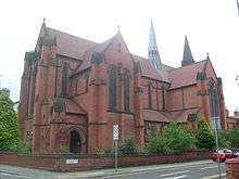 A bulky red brick church with two spirelets