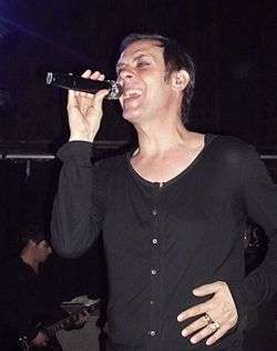 A short-haired man sings into a microphone.