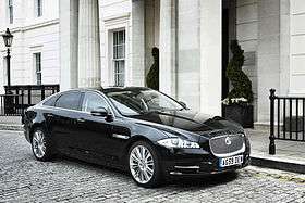 A black Jaguar XJ Sentinel parked stationary on a cobbled street in front of a white building.