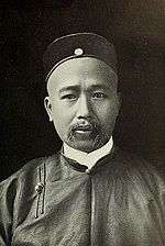 A Chinese man with a shaved head and mustache wearing formal attire.