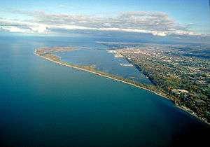 An aerial view of a thin, green peninsula arching into a large lake.