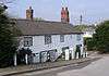 A long cottage in two storeys with tall chimneys and windows with intricate white-painted tracery.