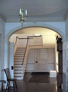 A photograph of the main stairway and hallway of a house, painted white.