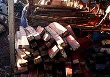 A stack of rosewood blanks sits in the foreground while a team of workers prepares additional timber in the background
