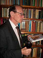 Professor Swanton holds a glass of wine in one hand and a copy of his book 'The Lives of Two Offas' in the other, at the launch of the book.