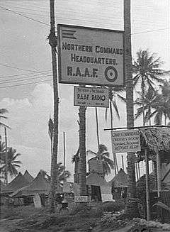 Palm trees, huts and sign reading "Northern Command Headquarters R.A.A.F."