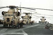 three sand painted RH-53 Sea Stallion helicopters sit on the flight deck of an aircraft carrier
