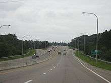 Uphill view of a four-lane divided freeway approaching an exit off-ramp