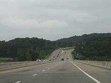 Downhill view of a four-lane divided freeway; the opposing lanes of traffic are separated by concrete barriers.