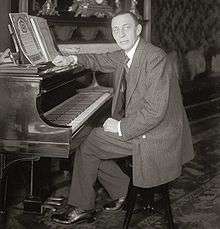Black and white photograph of a thin, clean-shaven man seated at a piano