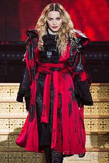 Madonna and her dancers dressed in Asian-inspired costumes in front of a blue backdrop.