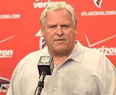 Candid photograph of Smith standing before a podium with a red backdrop bearing logos of the Atlanta Falcons and Verizon behind him