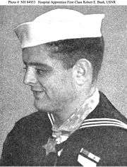Profile of a young white man wearing a white sailor's cap and a dark sailor suit. A star-shaped medal hangs from a wide ribbon around his neck.
