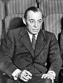Photo of Rodgers, in middle age, seated in a theatre, wearing a suit, and holding a cigarette
