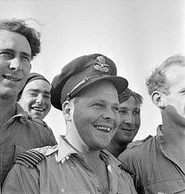 Informal head-and-shoulders portrait of grinning man in peaked cap surrounded by four others