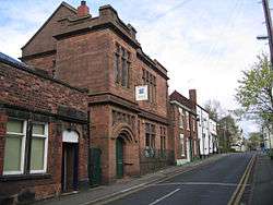A two-storey building in sandstone with an arched doorway, and mullioned and transomed windows