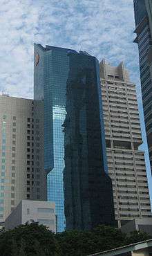 Distant ground-level view of a 40-story building with a blue glass facade; the building has a rectangular cross-section and a diaginal roofline.