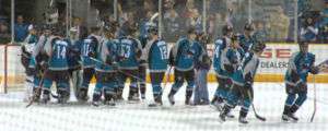Sharks team members lined up on the ice after a game congratulating their goaltender on a win.