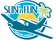 Logo depicts a small plane flying towards the viewer and facing the left. The background consists of two concentric circles (inner is yellow depicting the sun, outer is light blue to represent the sky). On the right is a palm tree and on the left (above the plane) is the name "SUN 'n FUN".
