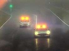 Two silver cars with amber and headlights on, driving in wet conditions