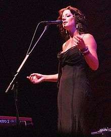 Woman wearing a black gown and singing in to a microphone.