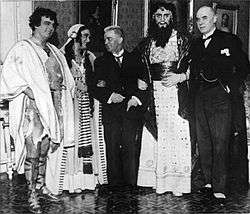 photopraph of Carl Nielsen in a suit linking arms with costumed members of the cast of Saul and David