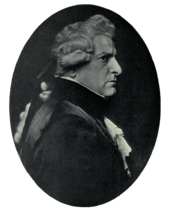  Right profile of stern-faced man in dark clothing with lacy shirt and cuffs, wearing a wig