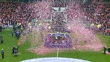Confetti rains around a platform in the middle of a football pitch