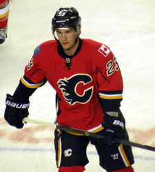 Upper body of a hockey player who is skating up the ice. He is in a red uniform with black and yellow trim, and a stylized "C" logo on his chest.