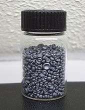 A small glass jar filled with small dull grey concave buttons. The pieces of selenium look like tiny mushrooms without their stems.