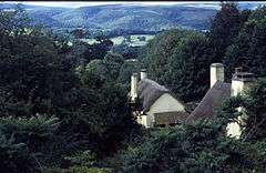 Thatched roofs of white painted houses nestled in tree filled valley.