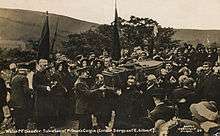 A Salvation Army funeral cortege, with men carrying the coffin. The streets are lined with people, some of whom have Salvation Army banners.