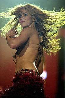 Shakira wearing a beige bra and a red skirt, with her hair twirling mid-dance