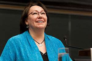 A colour photo of Sheila Watt-Cloutier, looking up and smiling, while giving a lecture at York University. She is a wearing a blue jacket over a black shirt and has an ulu necklace.
