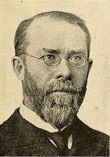 Stern-looking man with beard and round spectacles