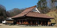 Wooden building with a hip-and-gable style roof and an open veranda surrounding the building.