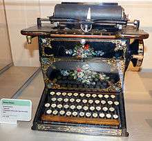 An ornately decorated typewriter with black lacquer, gold detailing and various floral arrangements