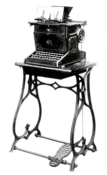 A black typewriter decorated with ornate floral patterns sits affixed to an iron sewing machine stand with a treadle.