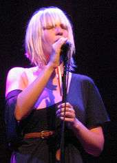 A blonde woman singing with her eyes closed