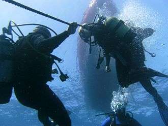 A group of divers seen from below. Two are holding onto the anchor cable as an aid to depth control during a decompression stop.