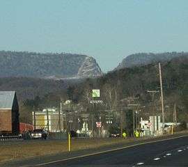 A small town is seen below a mountain ridge which contains a deep V-shaped cut.