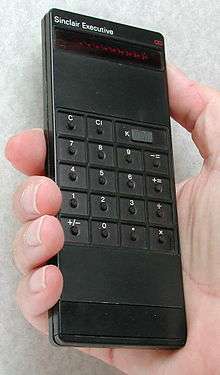 A black rectangular calculator being held in a person's right hand.