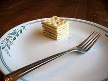 A plate, with a fork in the foreground and a stack of crackers in the background