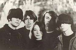 A sepia image of one female and four males standing against a distorted backdrop.