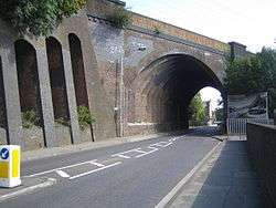 View along a narrow road, across which a brick arch carries a railway line at an oblique angle
