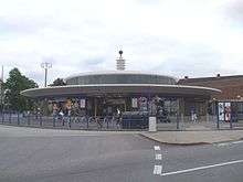 A low circular building with a wide awning is surmounted by a glazed column with a metal ball on the top