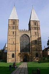 A simple Norman west front with two towers surmounted by short pyramidal spires. A large Gothic window has been inserted between the towers.