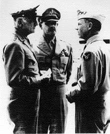 Three men in uniforms confer.