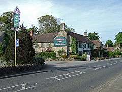 Building with pub sign saying the Sparkford Inn with car park and road in the foreground.